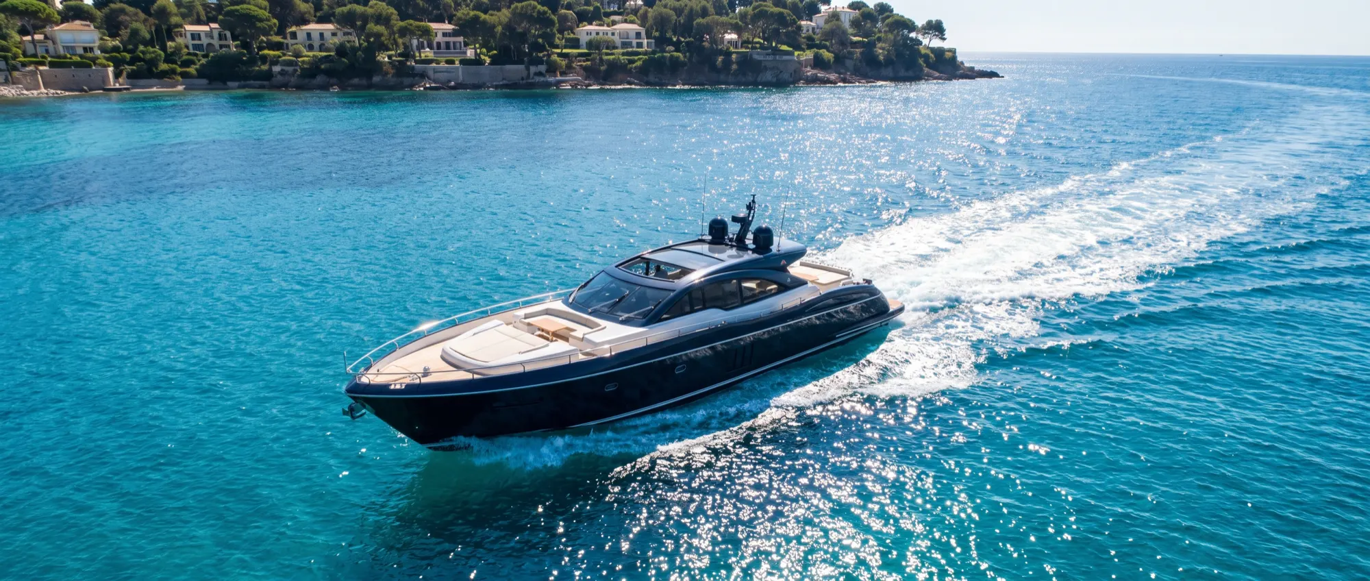 A navy sport yacht at speed across bright turquoise water off the Riviera coast.