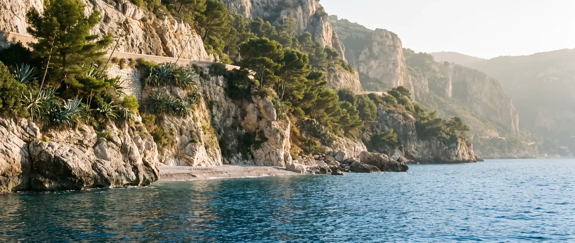 Cliffs below the corniche at Èze-sur-Mer with pines above deep blue water.