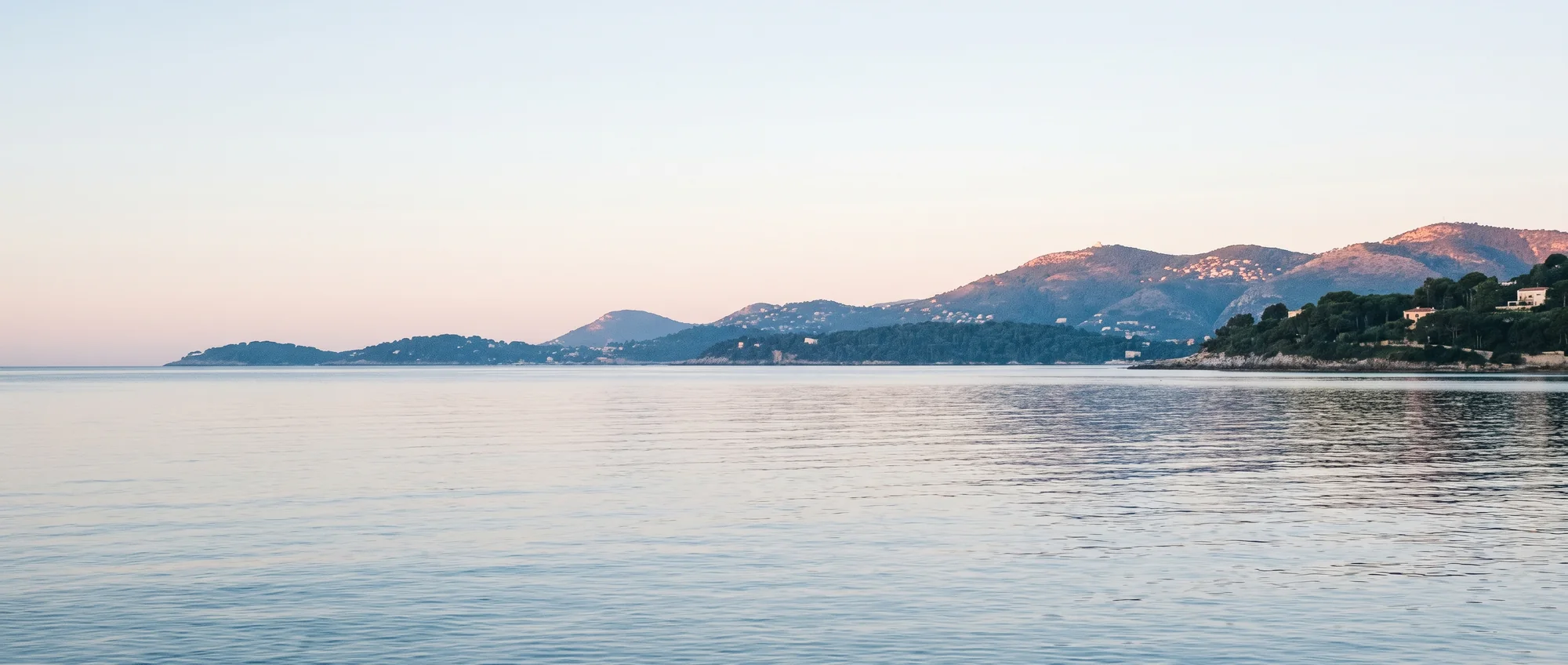 Flat glassy sea at first light with the coast low and blue behind it.