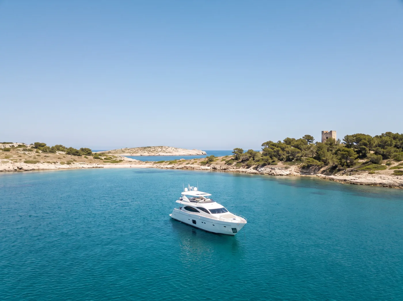 Un seul yacht au mouillage dans le large chenal entre les îles de Lérins, la vieille tour du fort parmi les pins.